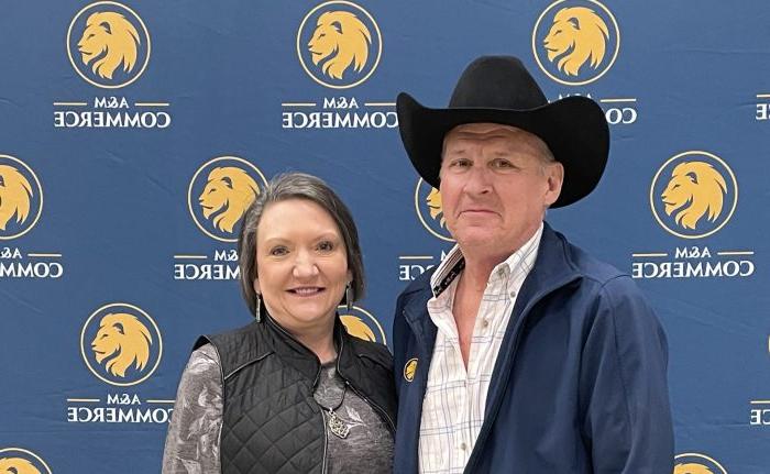 Scott and Margaret Stahl pose for a photo. Scott is wearing a black cowboy hat and the background is blue with several Lion head logos.